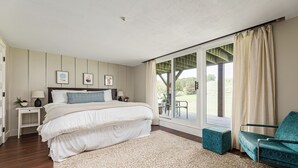 Une chambre avec un grand lit, une table de chevet, une chaise, une fenêtre avec des rideaux et une vue sur l’extérieur.