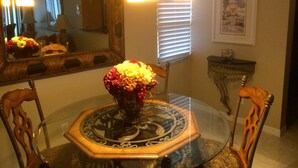 A dining area with a glass table, chairs, a vase of flowers, a mirror, and a framed picture on the wall. - Fairwinds Cove Florida Atlantic Ocean, Jensen Beach, Hutchinson’s Island, (Jensen Beach)
