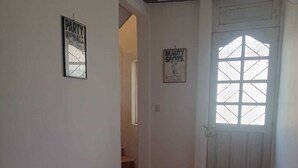 Um corredor com piso ladrilhado, uma porta com janela e dois cartazes nas paredes.
