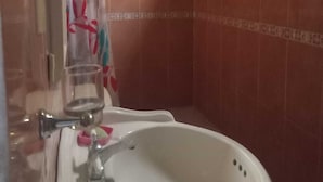 Casa de banho com lavatório branco, um copo de água e um separador de chuveiro com padrão floral.