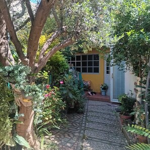 A narrow stone pathway leading to a yellow building with a window and a door. - Room in a family home (Oaxaca de Juárez)