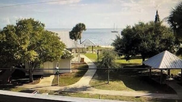 A residential area with a pathway leading to a house, a boat in the water, and a clear sky. - Lazy Shell Condo 325 (Cedar Key)