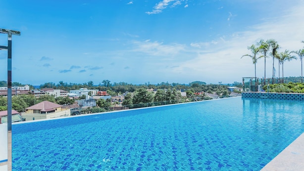 A clear blue pool with a view of a residential area and palm trees in the background. - Studio in Ozone Condo in Kata A702 (Karon)