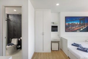 A modern hotel room with a large bed, a wardrobe, a small desk, and a bathroom with a toilet and shower.