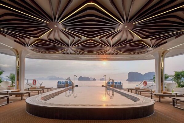 A spacious indoor pool area with a curved design, surrounded by seating and a view of the sea.