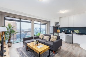 A modern apartment with a grey sofa, wooden coffee table, and a city view through large windows.