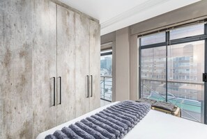 Una camera da letto con un ampio armadio, un letto con un tappeto soffice e vista sulla città attraverso ampie finestre.