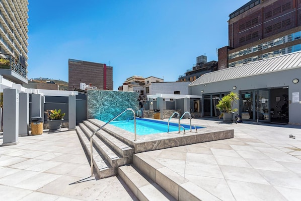 A rooftop pool with a clear blue sky in the background, surrounded by modern buildings.