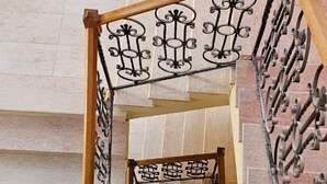 A staircase with a wooden handrail and black metal balusters, leading to a landing with a tiled floor. - Broadway Boutique Hotel (Tirana)