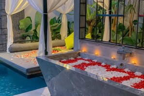 A spa area with a large bathtub filled with rose petals, a seating area with cushions, and a pool. - Vinna Villa Seminyak by The Wina Resorts (Bali)