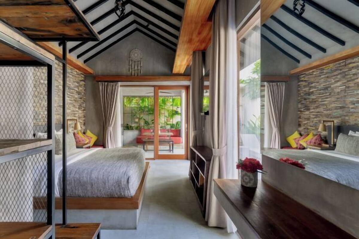 A bedroom with a bed, a small table, and a bench. There is a sliding glass door leading to an outdoor area.