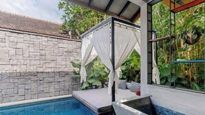 A swimming pool with a stone wall, a glass enclosure with curtains, and a tiled area. - Vinna Villa Seminyak by The Wina Resorts (Bali)