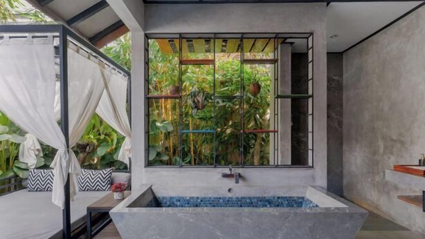 A modern bathroom with a freestanding bathtub, a window with a view of greenery, and a shower area. - Vinna Villa Seminyak by The Wina Resorts (Bali)