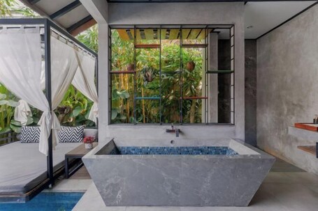 A modern bathroom with a freestanding bathtub, a window with a view of greenery, and a shower area.