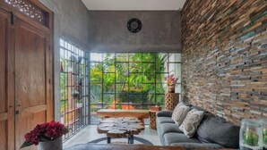 A modern living room with a wooden coffee table, a sofa, and a view of greenery through large windows. - Vinna Villa Seminyak by The Wina Resorts (Bali)