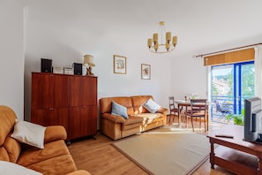 A living room with a sofa, a wooden cabinet, a chandelier, and a dining area with a table and chairs.