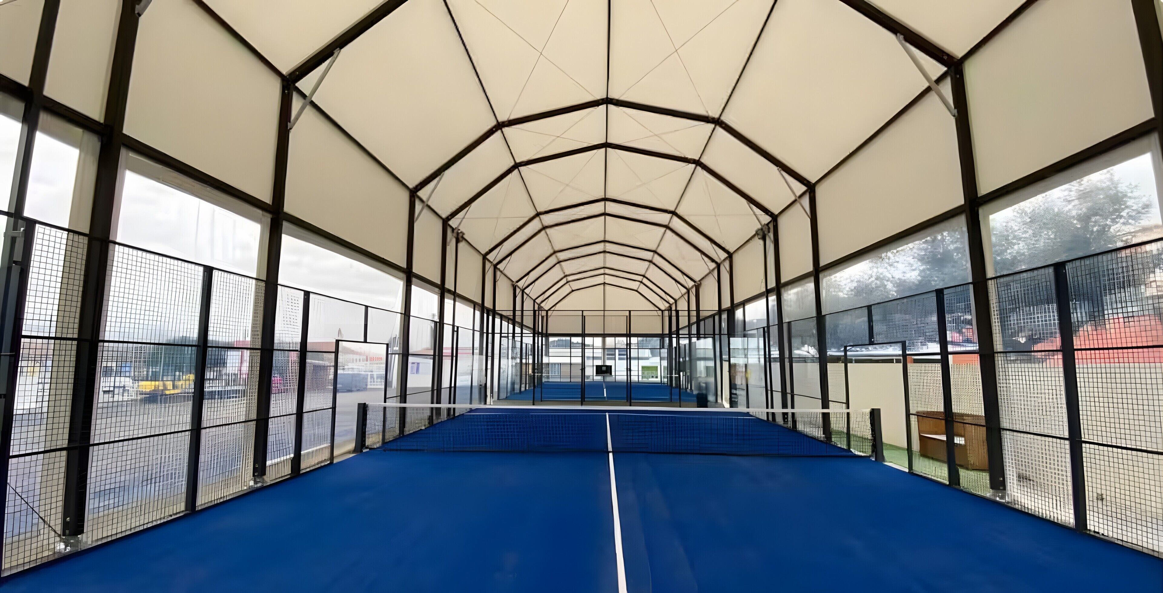 An indoor sports facility with a blue floor, netted walls, and a high ceiling.