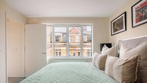 Ein Schlafzimmer mit großem Fenster, einem Bett mit Steppdecke und einem Heizkörper.