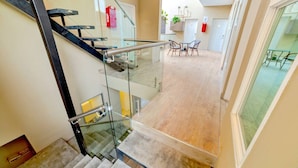 A modern interior with a glass staircase, a dining area with chairs and a table, and a visible fire extinguisher. - MarvelousStudio KingBed - 10minWalkToBorder (Tijuana)