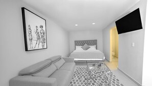 A modern hotel room with a bed, a sofa, a coffee table, and a TV mounted on the wall. - MarvelousStudio KingBed - 10minWalkToBorder (Tijuana)