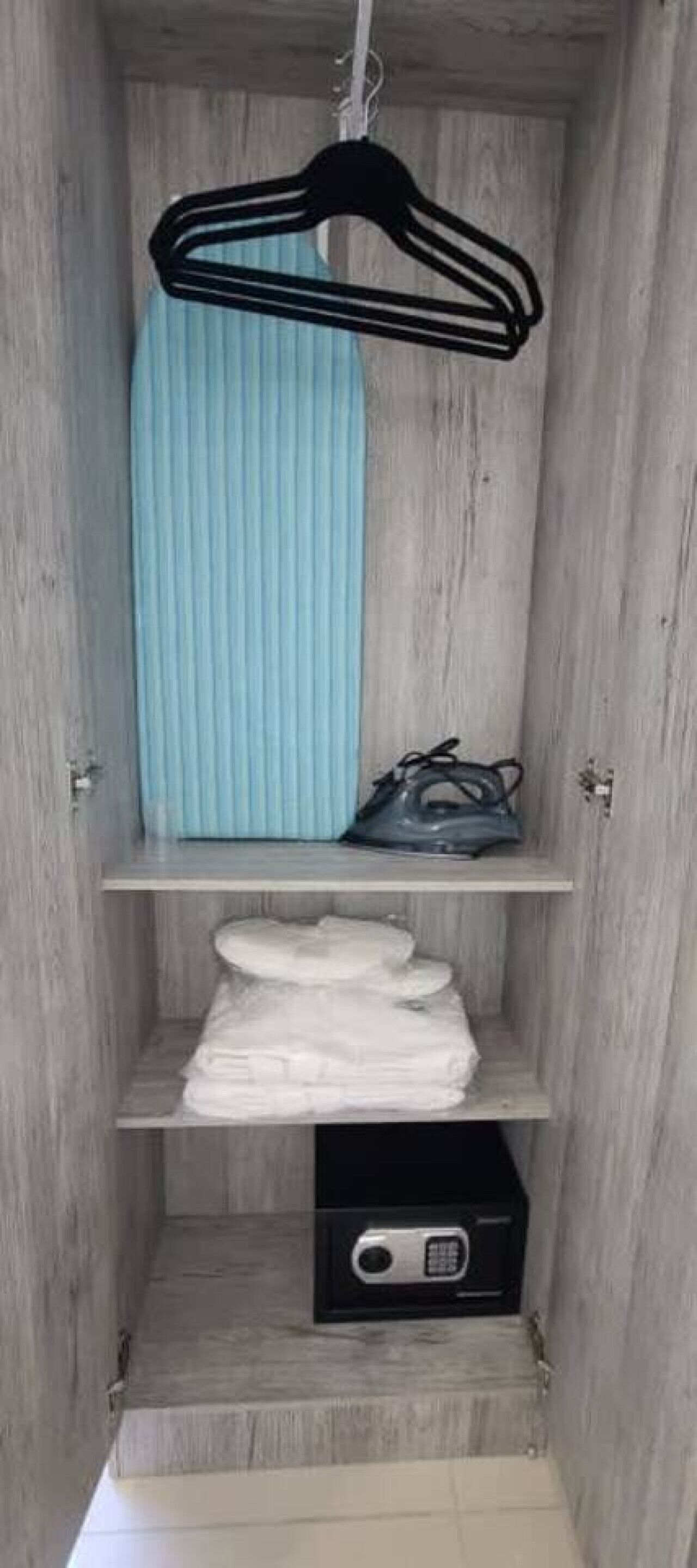 A wooden closet with a hanging rack, a shelf with folded clothes, and a black storage box.