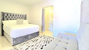 A modern bedroom with a large bed, a grey upholstered headboard, a white sofa, and a patterned rug. - Nice Studio Close to PedEast/West (Tijuana)