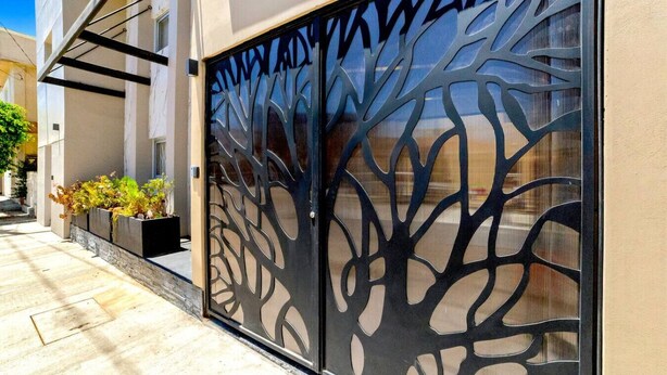 A modern building with a decorative metal gate featuring tree-like patterns. - KingBed+CouchBed-NearD`Border (Tijuana)