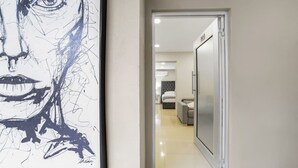 A hallway with a framed artwork on the left and a doorway leading to a room with a bed and a bedside table. - KingBed+CouchBed-NearD`Border (Tijuana)