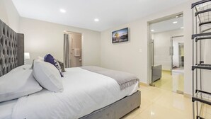 A modern hotel room with a large bed, a grey headboard, a painting on the wall, and a view of the hallway. - KingBed+CouchBed-NearD`Border (Tijuana)