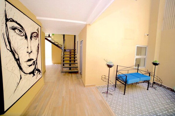 A hallway with a staircase, a bed with a blue mattress, and a large abstract painting on the wall.