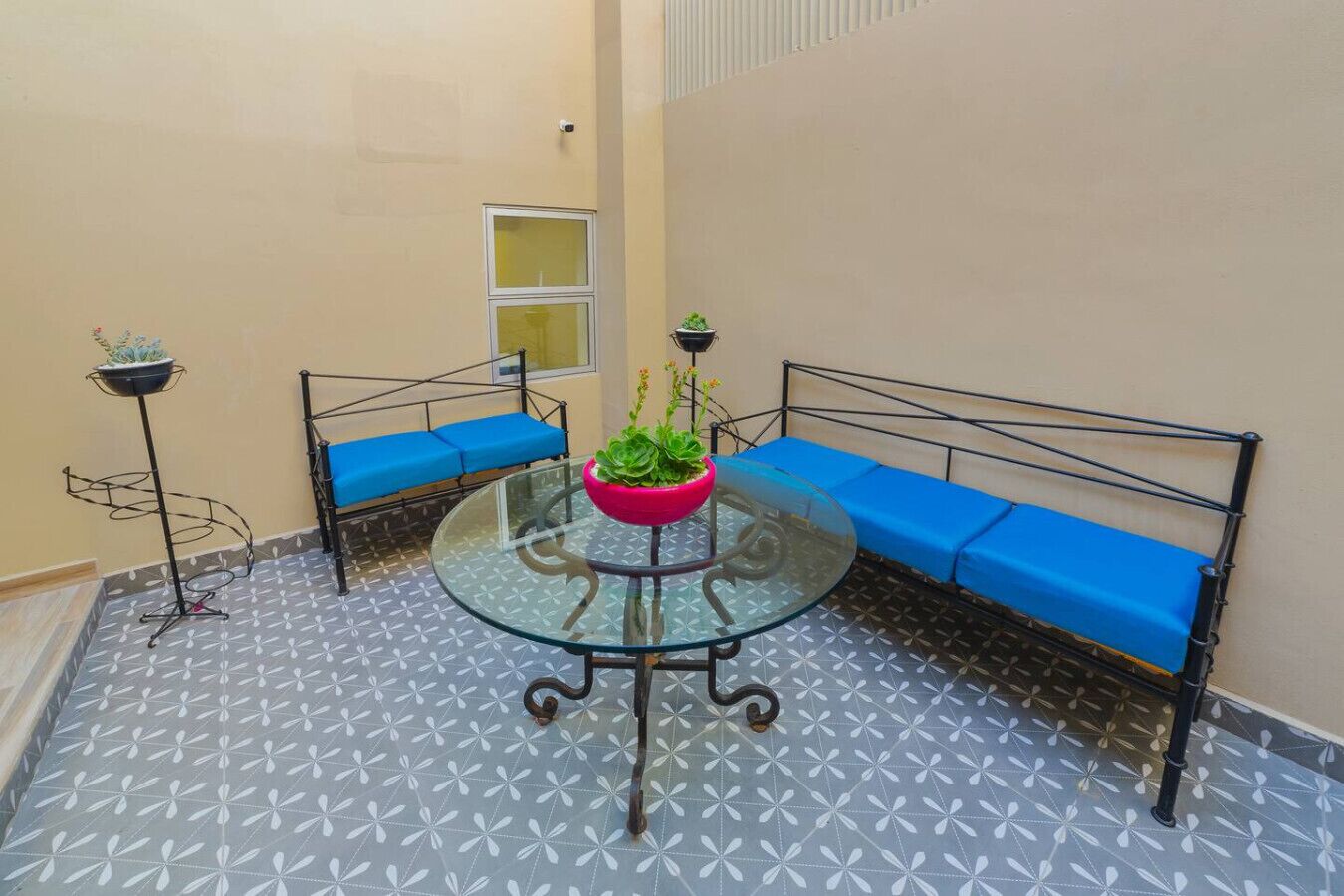 Un pequeño patio cerrado con una mesa de vidrio rodeada de bancos acolchados azules.