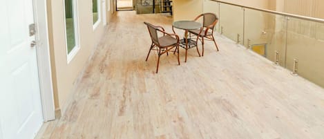 A spacious hallway with a wooden floor, a glass railing, and a table with chairs.