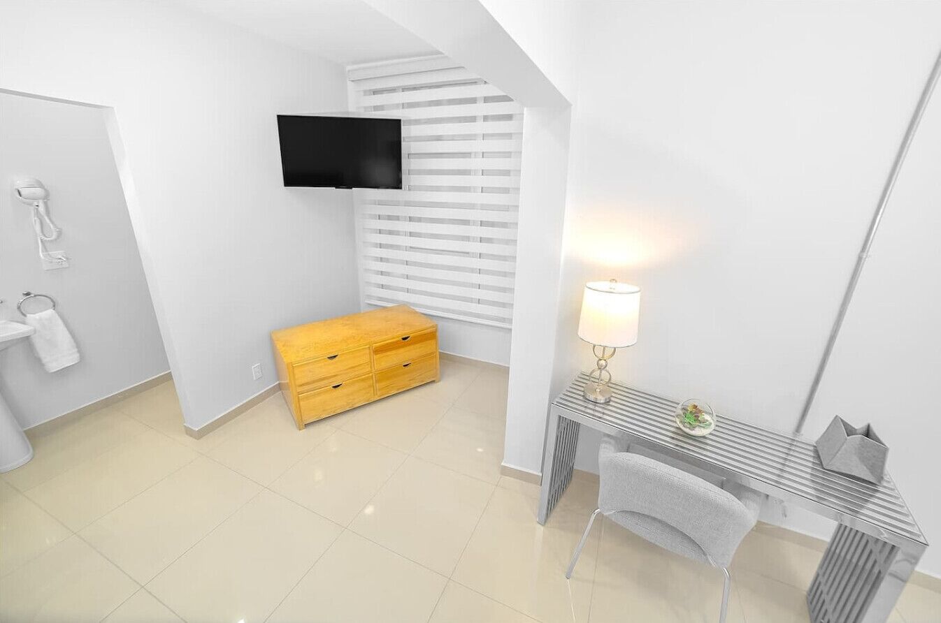 A modern bathroom with a wooden chest of drawers, a vanity with a mirror, and a wall-mounted TV.
