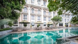 A swimming pool with lounge chairs and umbrellas, surrounded by a building with large windows and a classic architectural style. - Cozrum Homes - Sonata Residence (Ho Chi Minh City)