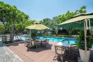 A poolside area with lounge chairs, umbrellas, and a wooden deck. - Cozrum Homes - Sonata Residence (Ho Chi Minh City)