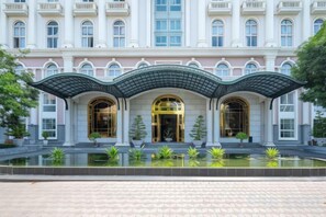 A hotel with a grand entrance, a covered walkway, and a reflective water feature in front. - Cozrum Homes - Sonata Residence (Ho Chi Minh City)