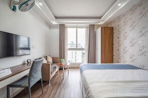 A hotel room with a bed, a desk, a chair, a small table, a TV, and a window with curtains. - Cozrum Homes - Sonata Residence (Ho Chi Minh City)