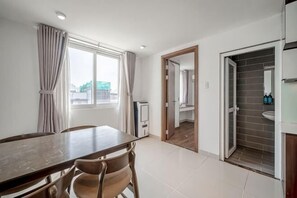 A room with a dining table, chairs, a window with curtains, a door leading to a bathroom, and a tiled floor. - Cozrum Homes - Sonata Residence (Ho Chi Minh City)