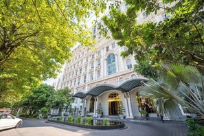 A hotel with a classical facade, a curved entrance, and a landscaped garden. - Cozrum Homes - Sonata Residence (Ho Chi Minh City)