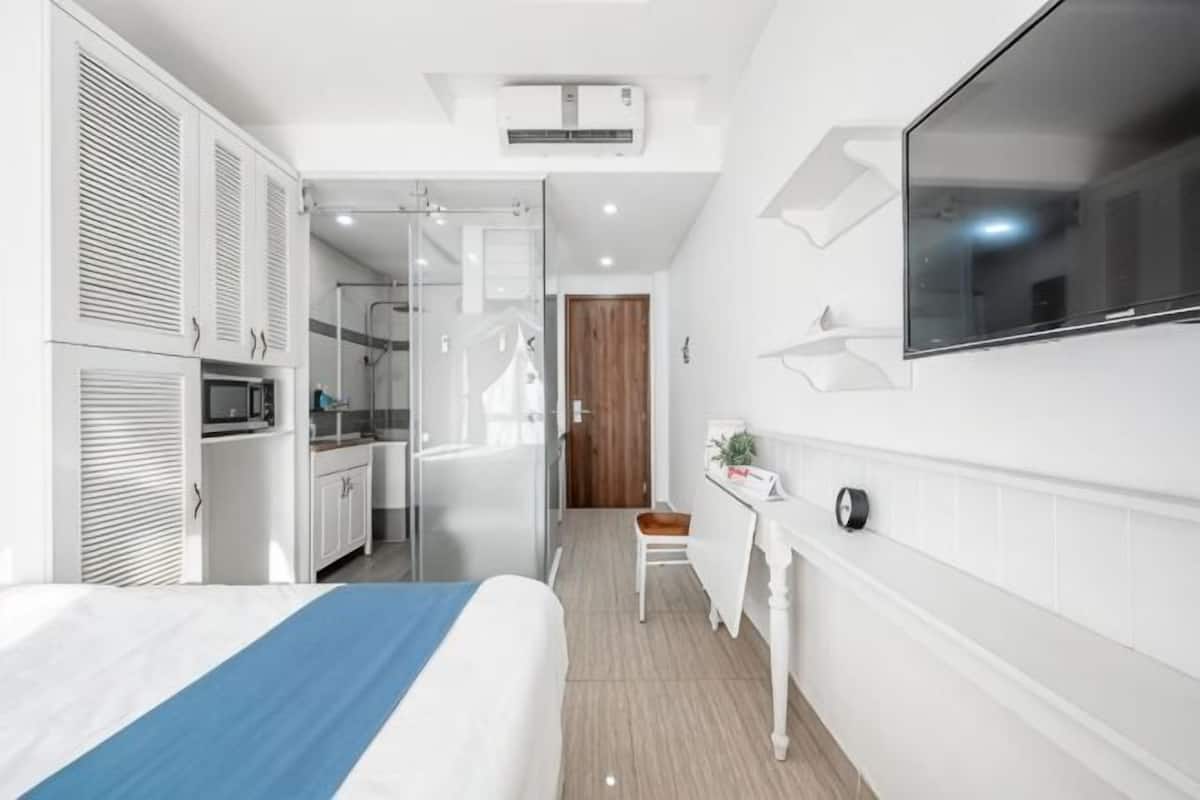 Ein modernes Hotelzimmer mit Bett, Schreibtisch, Stuhl, Fernseher und einer Küchenzeile.