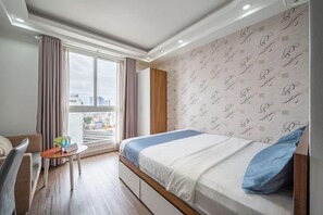 A hotel room with a bed, a desk, a chair, and a window with curtains. - Cozrum Homes - Sonata Residence (Ho Chi Minh City)
