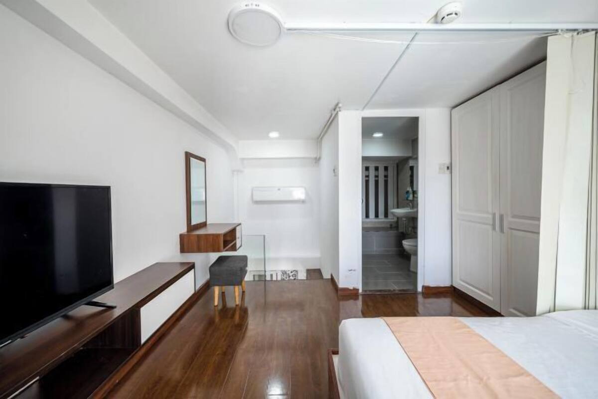 Ein modernes Hotelzimmer mit Flachbildfernseher, Holzmöbeln, einem Bett, einem Schreibtisch und einem Kleiderschrank.