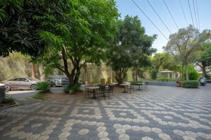 Un espace extérieur aménagé en terrasse, avec un sol à motifs hexagonaux, des tables, des chaises et une voiture garée à proximité.