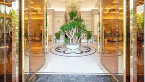A luxurious hotel lobby with a central potted plant, a chandelier, and a marble floor. - Cozrum Homes - Sonata Residence (Ho Chi Minh City)
