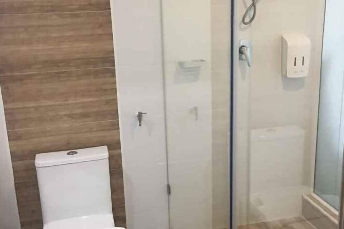 A bathroom with a toilet, a glass-enclosed shower, and a wall-mounted soap dispenser.