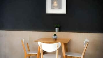 A dining area with a wooden table and white chairs, a framed picture on the wall, and a small potted plant on the table.