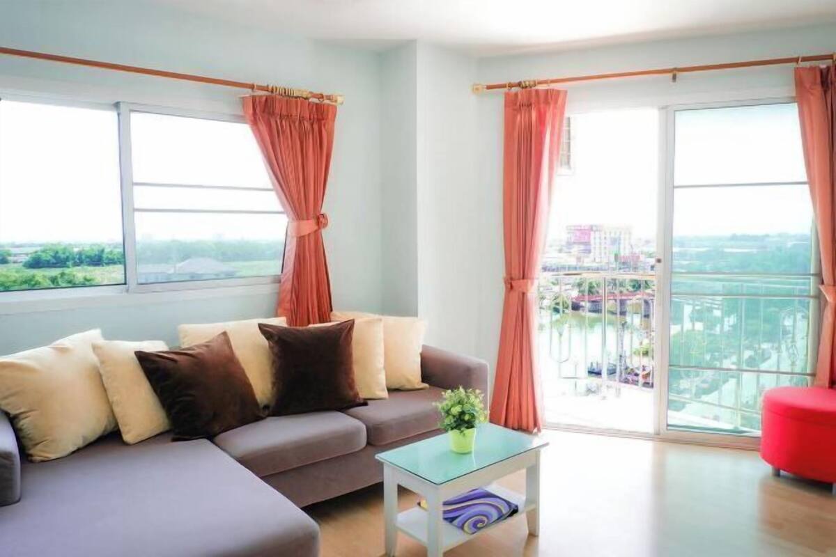A modern living room with a sofa, a small table with a plant, and large windows with curtains.