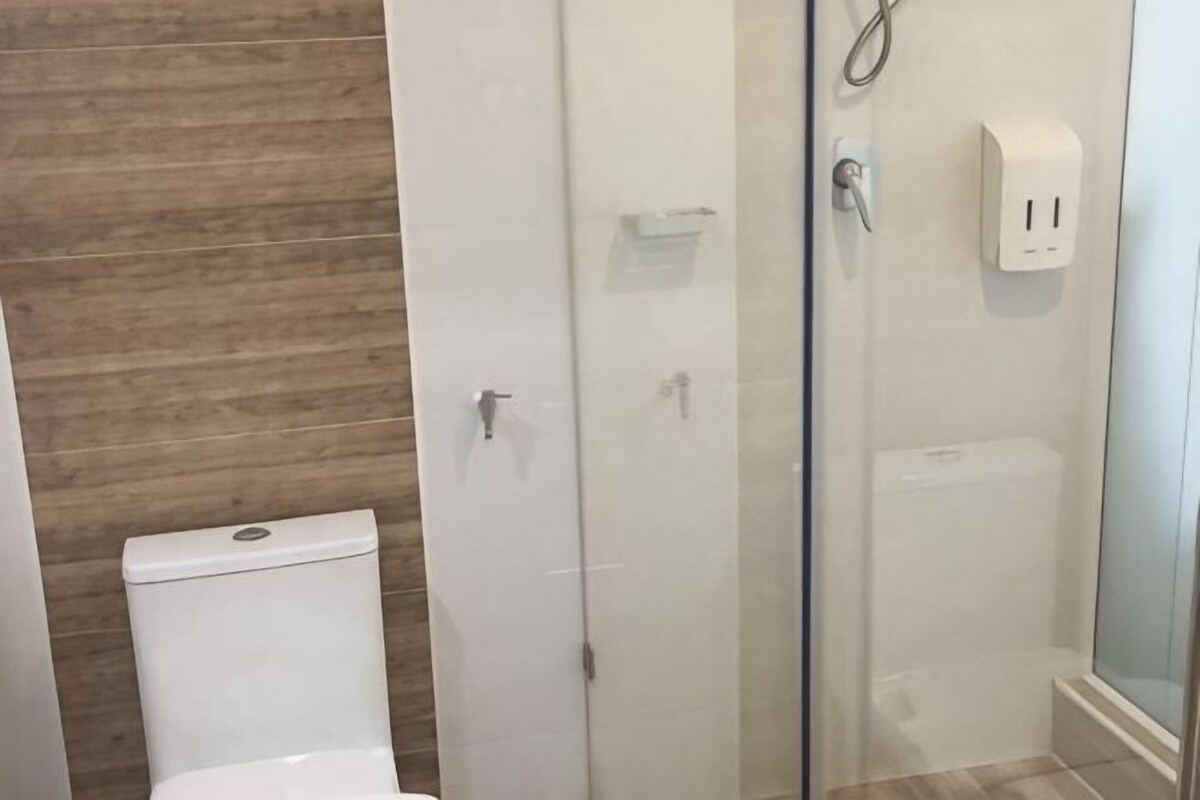 A bathroom with a toilet, a glass shower enclosure, and a wall-mounted soap dispenser.