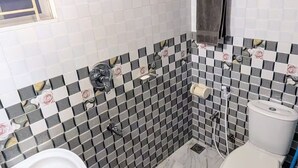 Casa de banho com lavatório branco, sanita e área de duche. As paredes são revestidas a mosaico xadrez e o chão é de mármore.