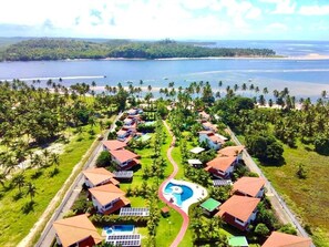 Un complexe hôtelier comprenant plusieurs bâtiments de style bungalow, une piscine centrale et offrant une vue sur l’océan et la végétation environnante.